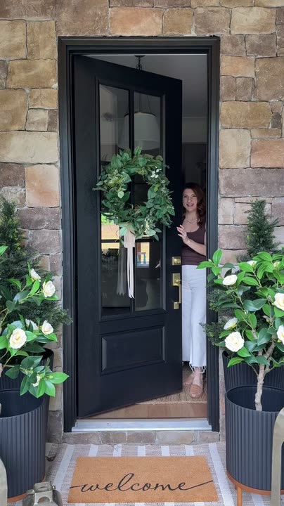 Reel by @coryell.home: Black full-glass front door with a green wreath between potted olive trees on a stone entry.