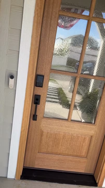 Reel by Kashia: Natural wood front door with six glass panes on a light house with flowers either side.
