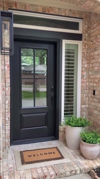 Reel by @linseywoods.home: Black front door with four glass panes on a brick house, a doormat and planter at the step.